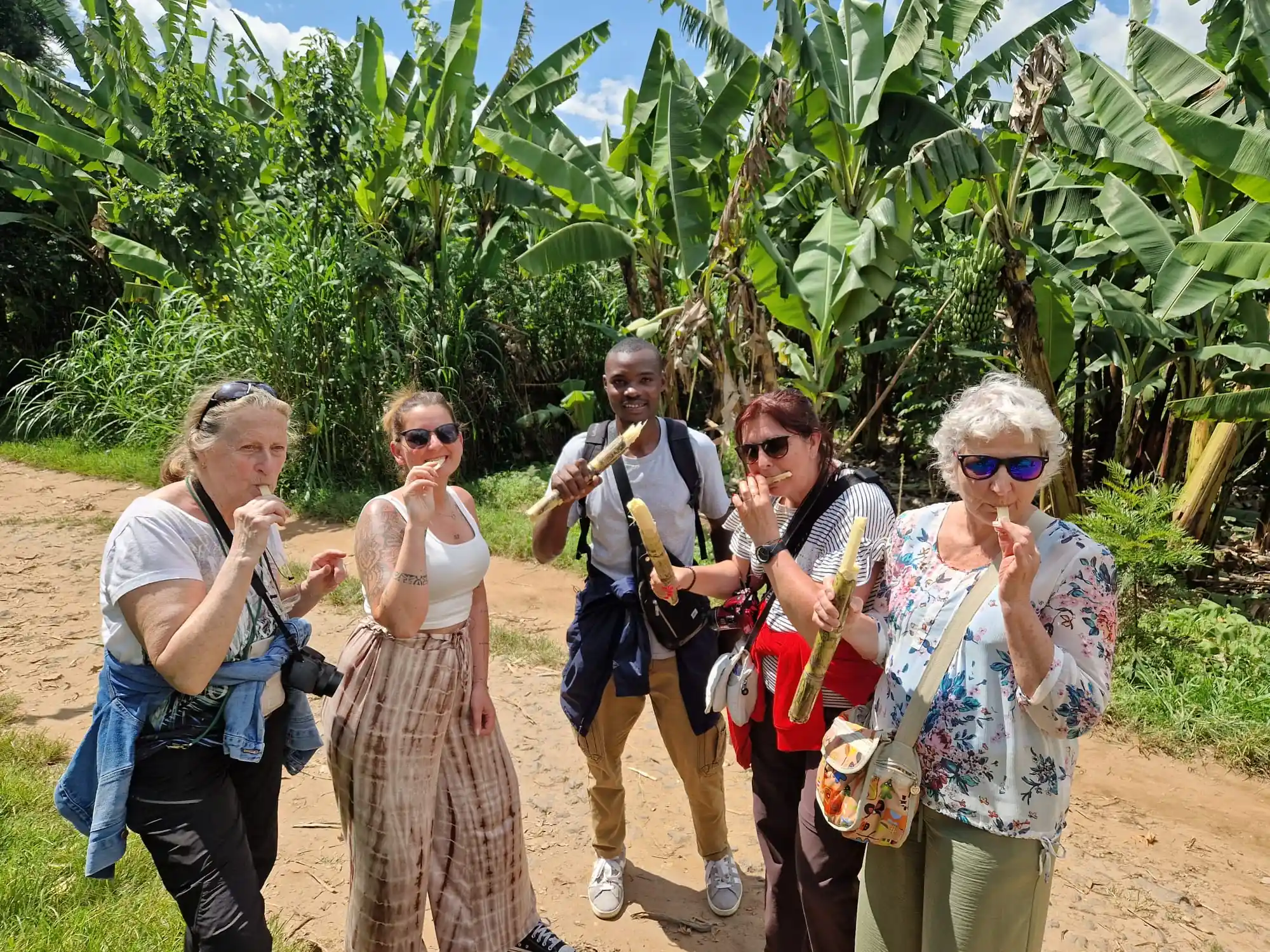 How to Experience Rwanda Like a Local – local Rwandan guide sharing fresh sugar cane with female travelers during an authentic cultural tour in rural Rwanda.