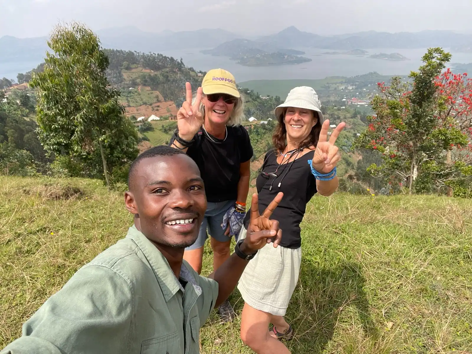 Local Rwandan guide and two women travelers take a joyful selfie after hiking the scenic hills overlooking Twin Lakes Burera and Ruhondo near Musanze, Rwanda.