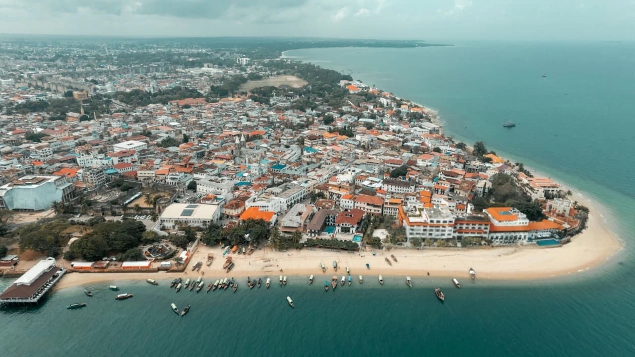 Aerial shot of Zanzibar paradise with Stone Town rooftops, turquoise coastline, boats, and vibrant greenery.”