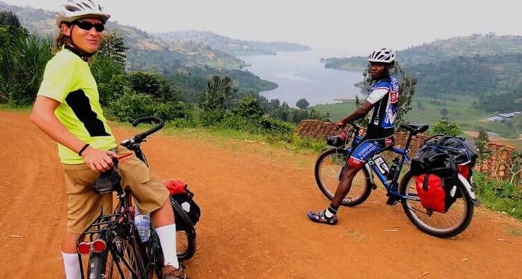 Two cyclists riding along the Congo Nile Trail in Rwanda on a scenic mountain path during a guided road cycling tour.