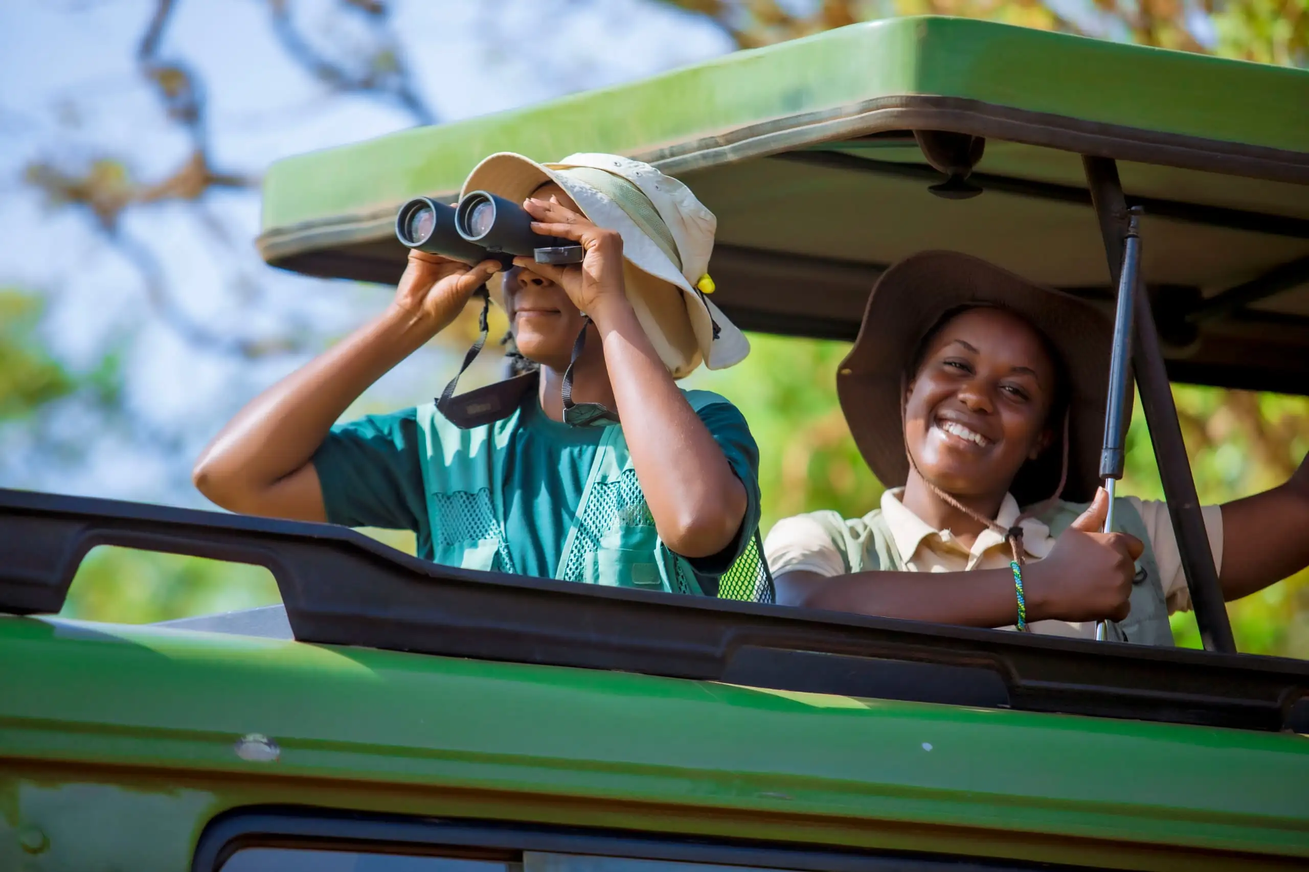 Female safari guides birdwatching inside a vehicle in Akagera National Park, spotting wildlife with binoculars – Best Places for Birdwatching in Uganda and Rwanda.