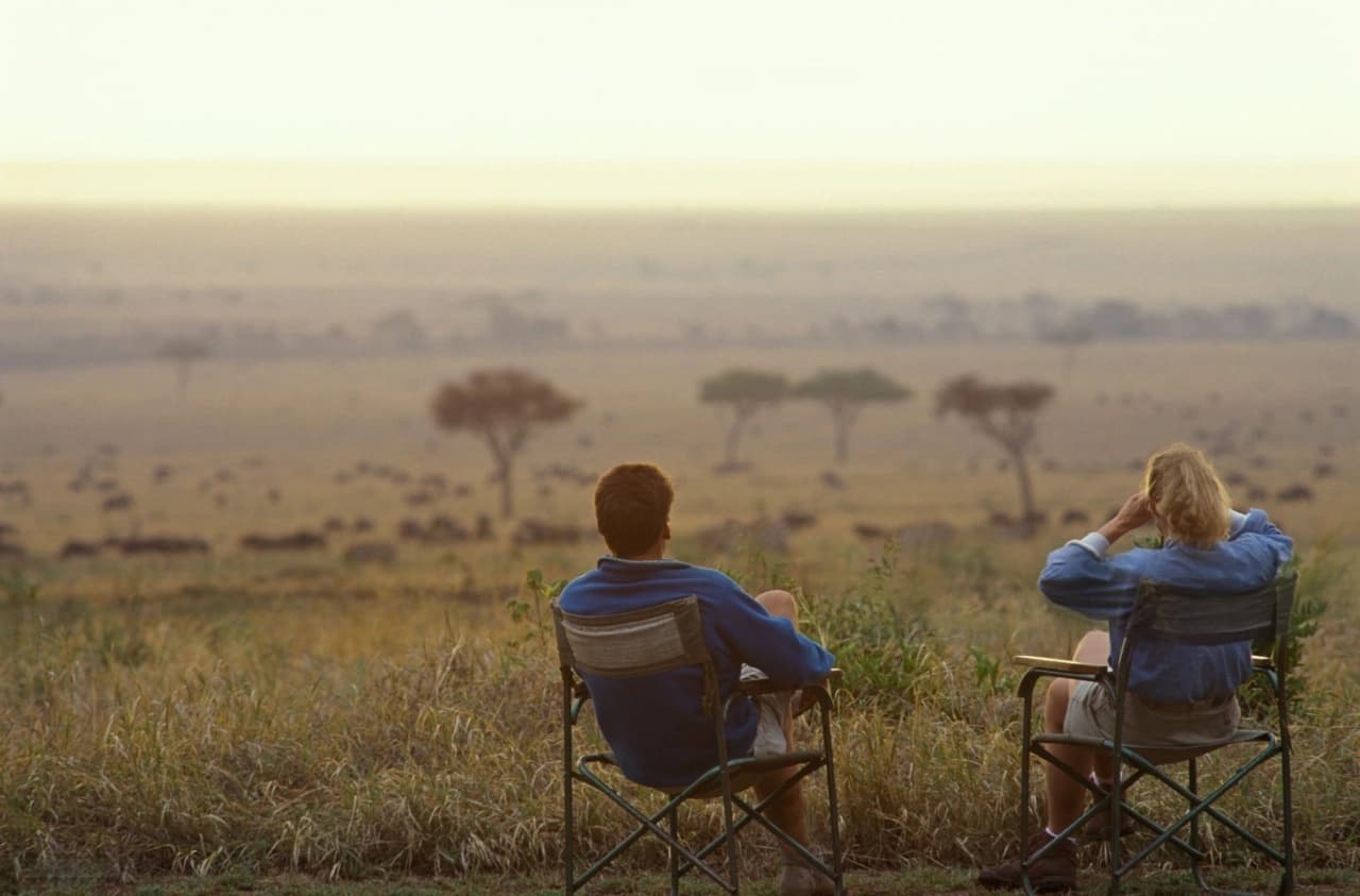 Two travelers sitting on camp chairs in the South African bush plains observing wildlife during an eco-luxury safari — how to plan South Africa eco luxury safari.