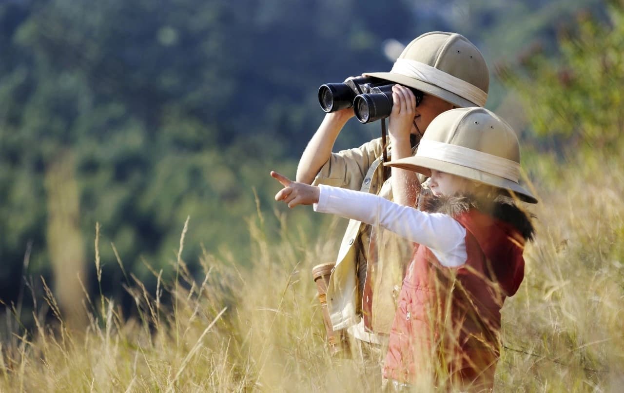 Two children on a family safari in the Tanzanian bush using binoculars to spot distant wildlife — Best family friendly safari and tours in Tanzania.