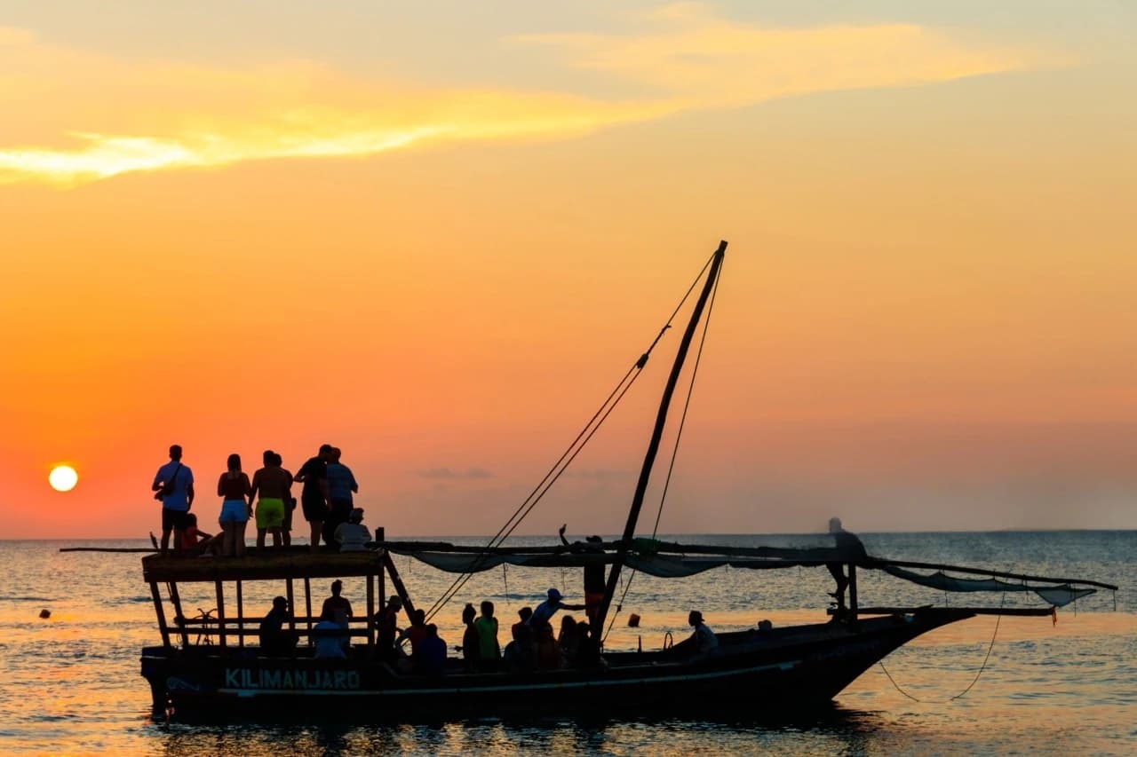 Traditional wooden dhow sailing across turquoise waters at sunset in Zanzibar paradise, showcasing the island’s serene coastline and tropical beauty.