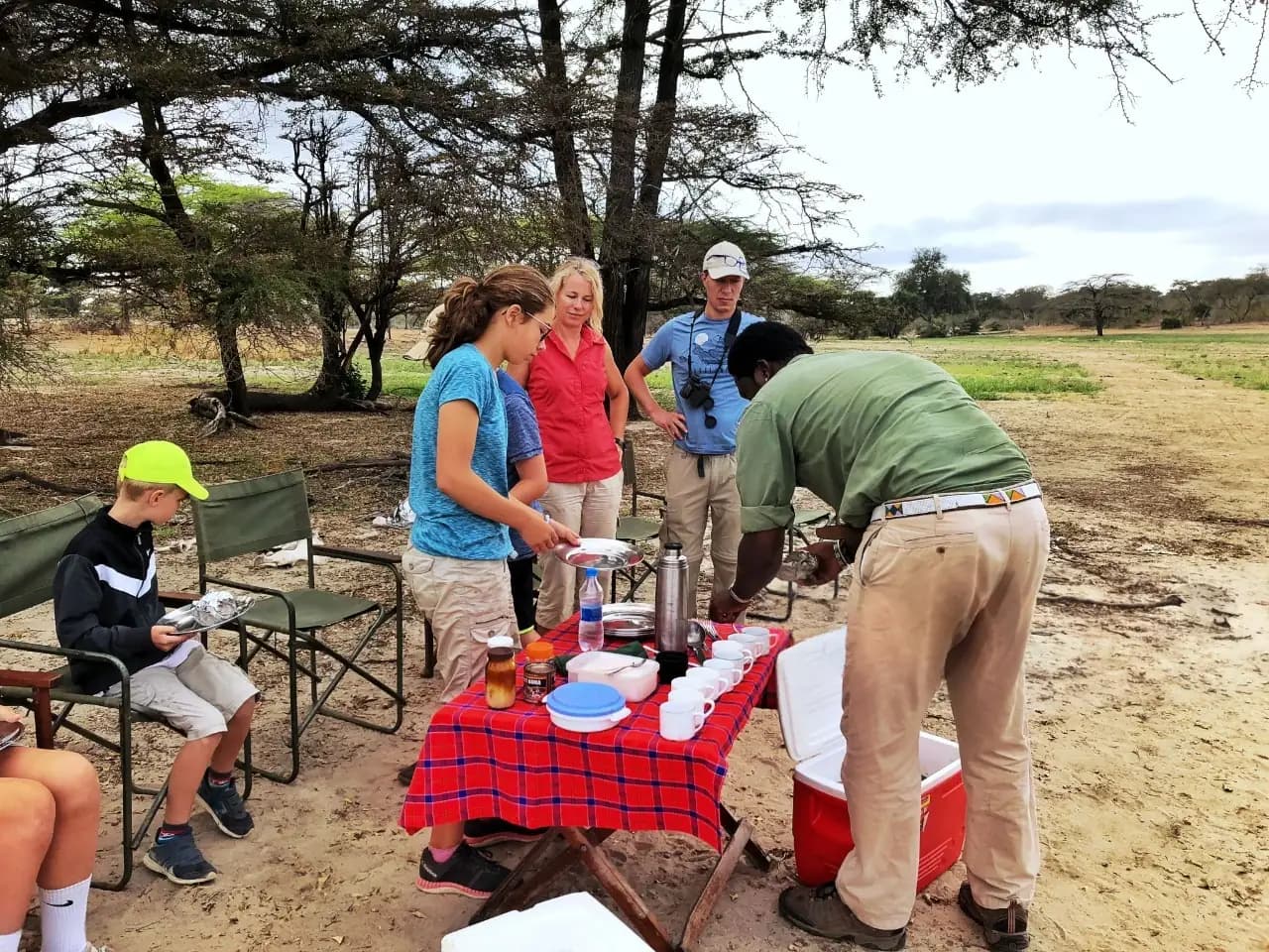 Family on a Tanzania bush safari walking to lunch as guides prepare a meal, showcasing the best family friendly safari and tours in Tanzania.