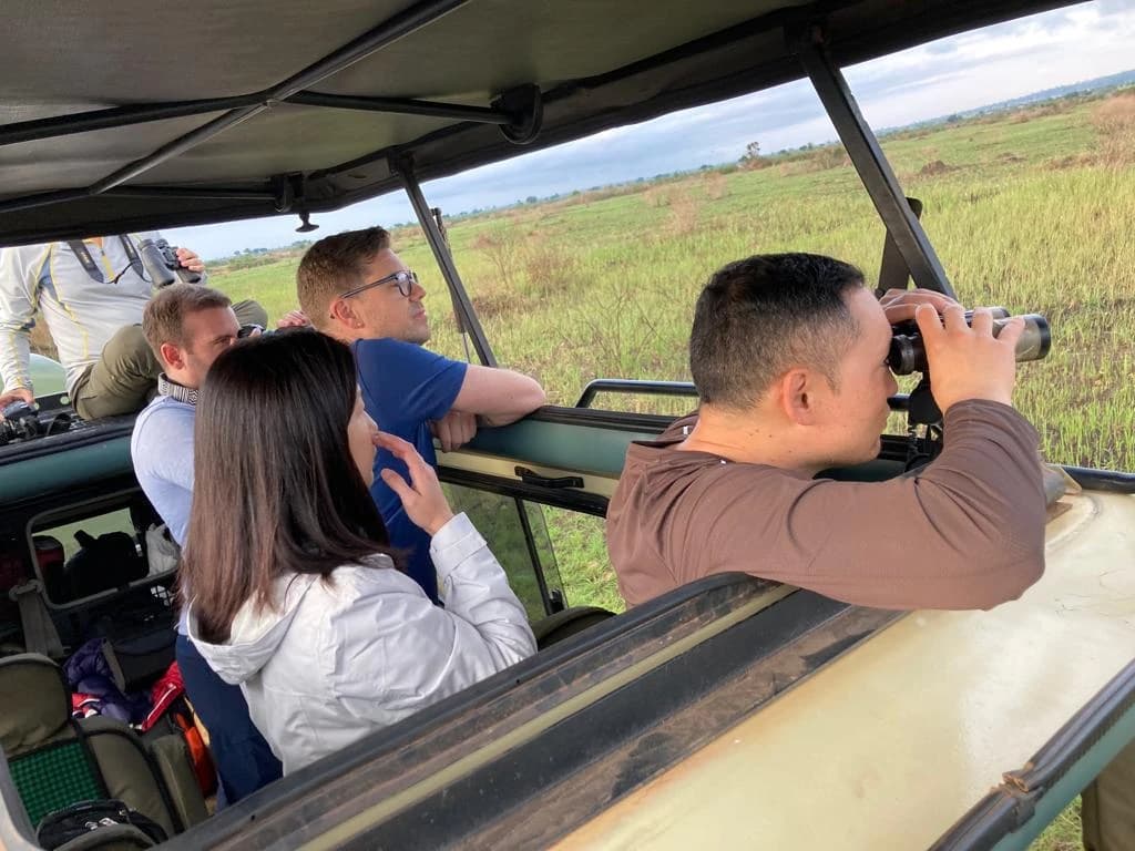 Tourists on Uganda safaris for families with Swift Africa Safaris expert local guide in Queen Elizabeth National Park, observing wildlife with binoculars and by naked eye during a cultural and wildlife tour.