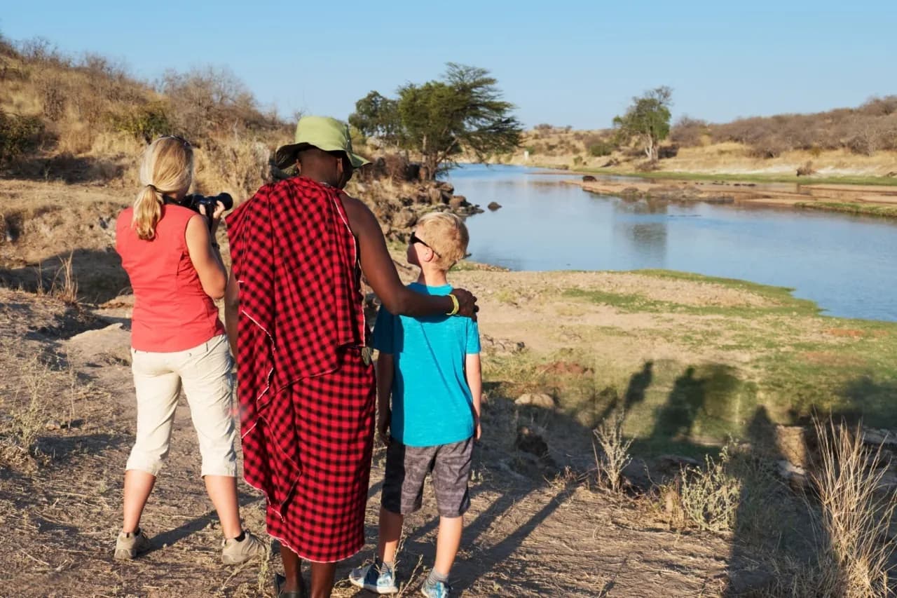 “A Maasai guide showing a Tanzanian landscape to a mother and her child during a family friendly safari tour in Tanzania — best family friendly safari and tours in Tanzania.