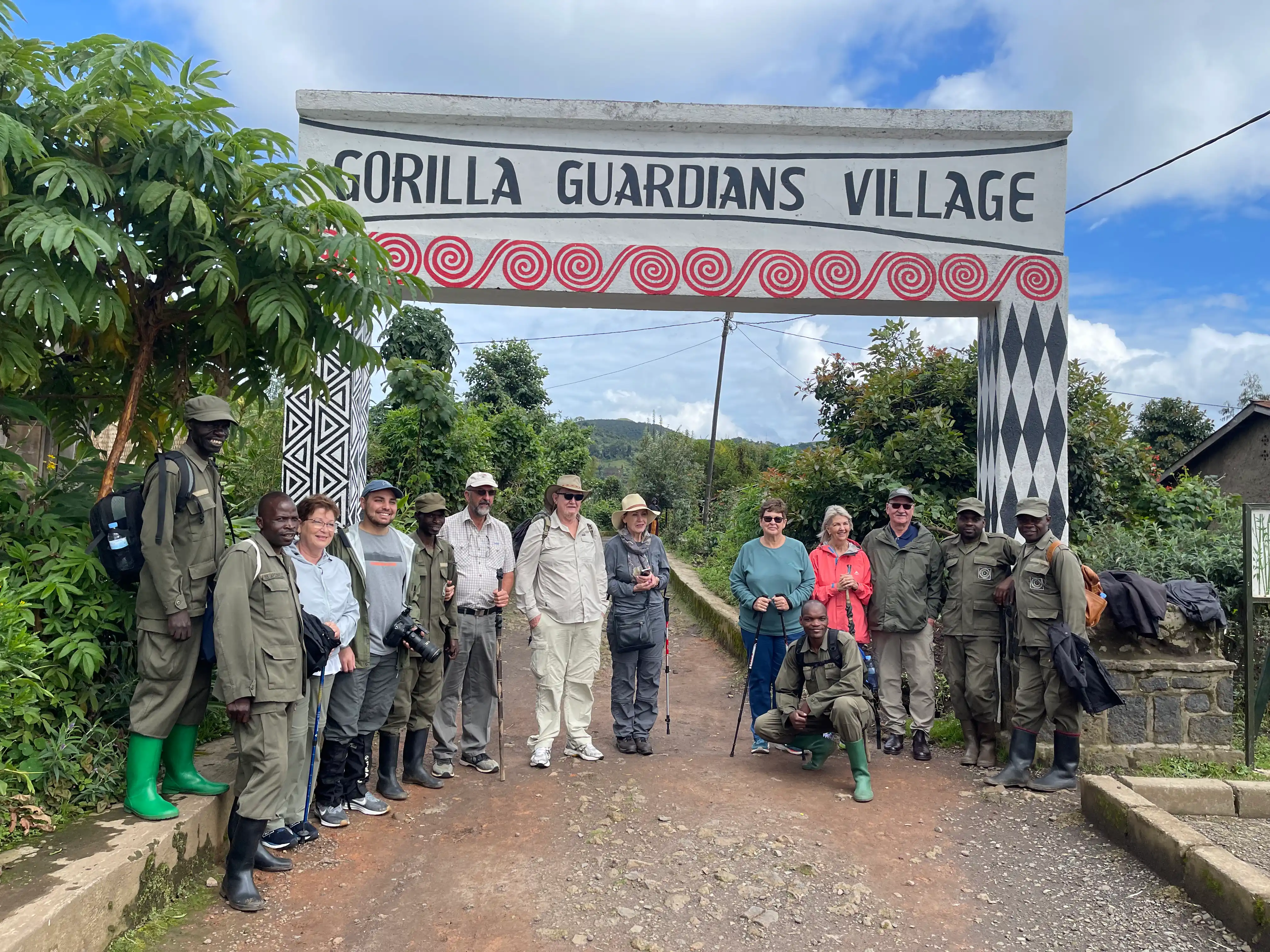 Travelers visiting Gorilla Guardians Village in Rwanda standing with their local host and guides at the village gate, celebrating Rwandan culture and community-based tourism.