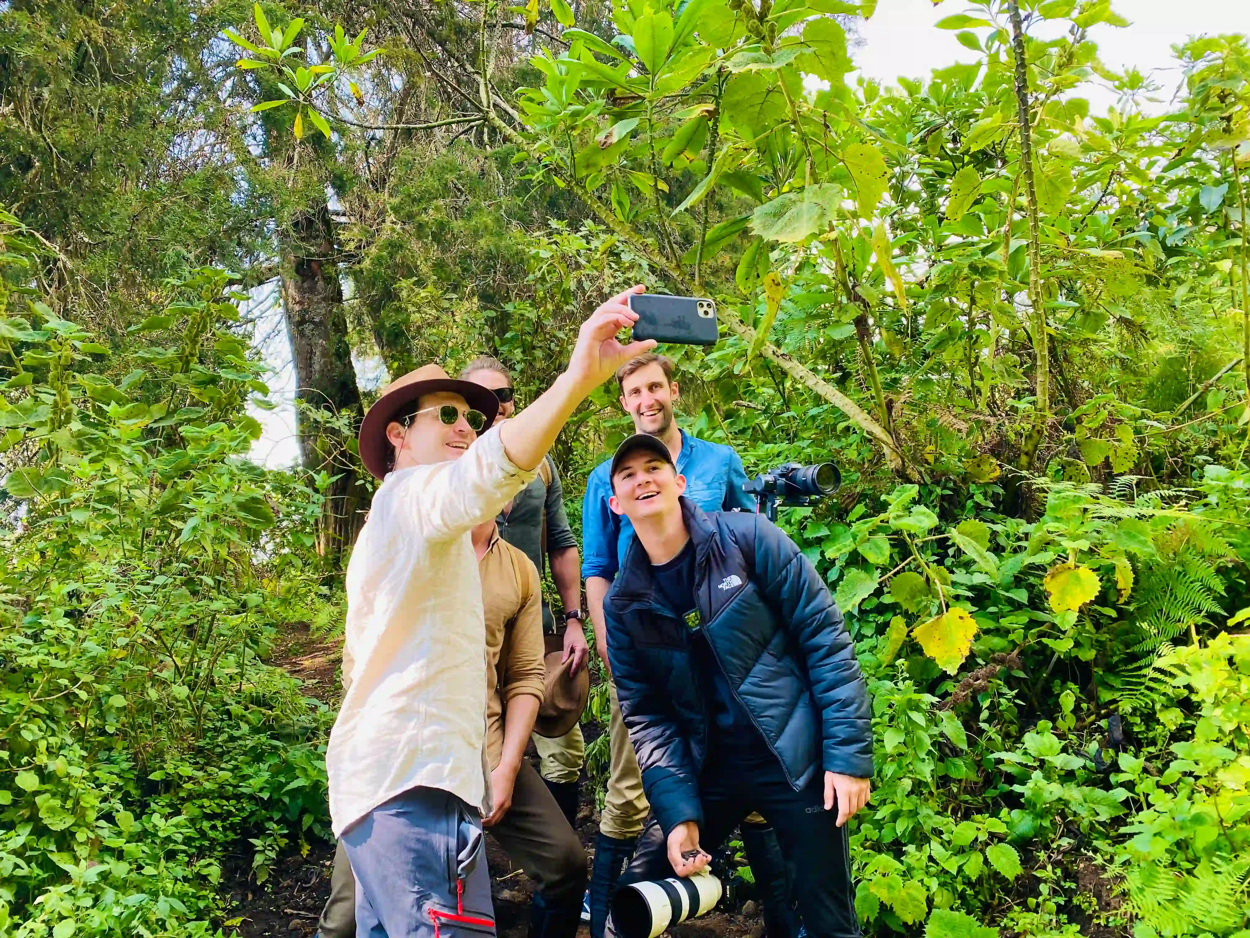 Group of travelers taking a selfie during Group Mountain Gorilla Trekking in Rwanda: The Ultimate Safari Experience, surrounded by the lush rainforest of Volcanoes National Park.
