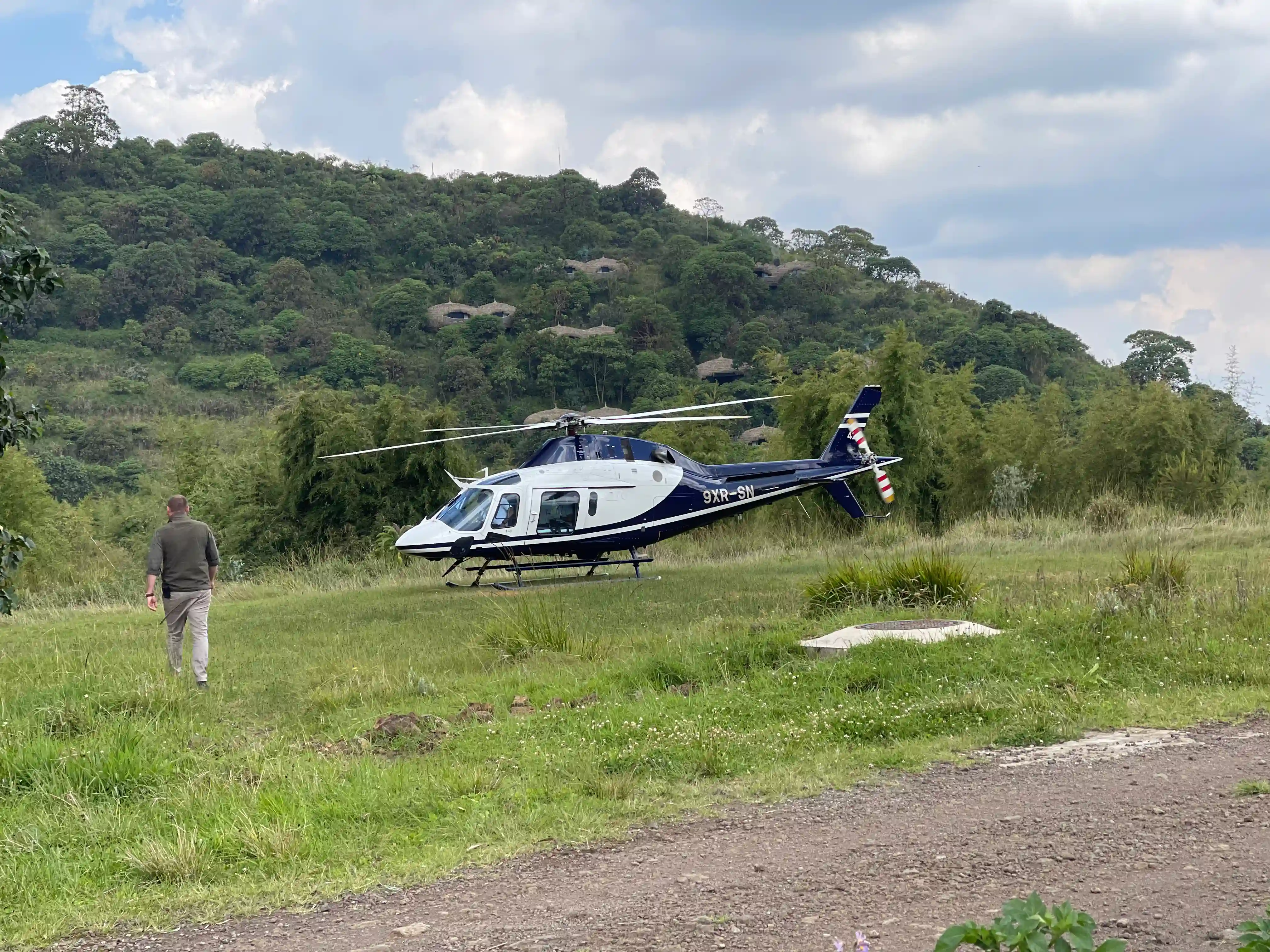 A luxury traveler boards a sleek private helicopter flying over Rwanda’s Volcanoes National Park, with misty rainforest, lush green hills, and the majestic Virunga volcanoes in the background — symbolizing an exclusive gorilla trekking adventure and upscale safari experience.