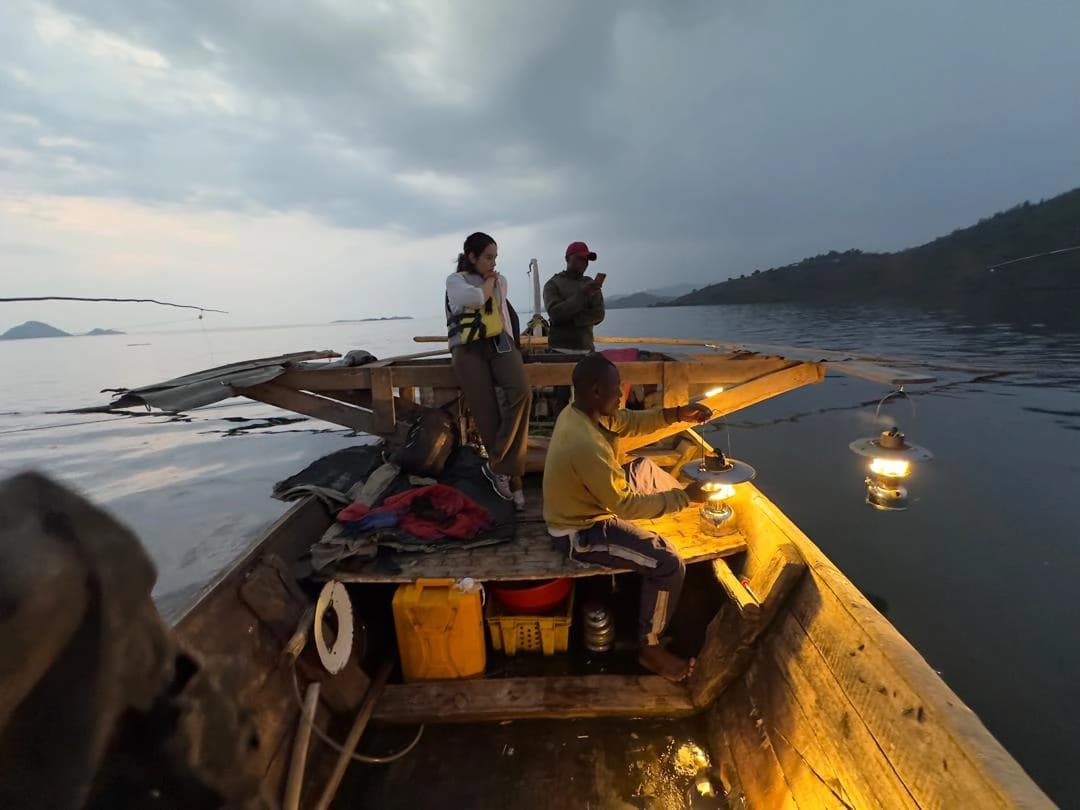 Local fishermen night fishing with a woman traveler in a traditional boat on Lake Kivu along the Congo Nile Trail, Rwanda — authentic cultural travel experience.