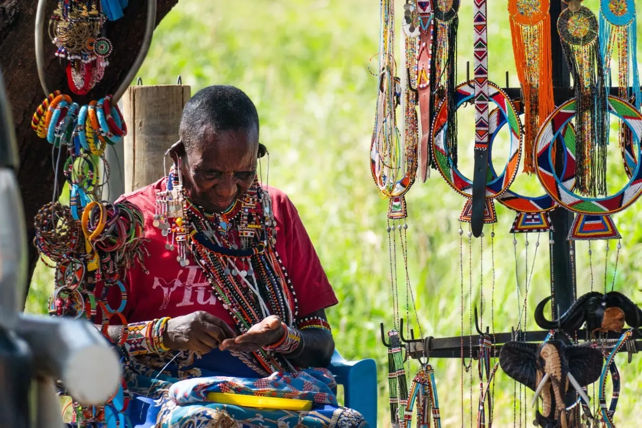 Maasai woman crafting traditional colorful beads in Kenya, showcasing cultural heritage and artisanal skill.