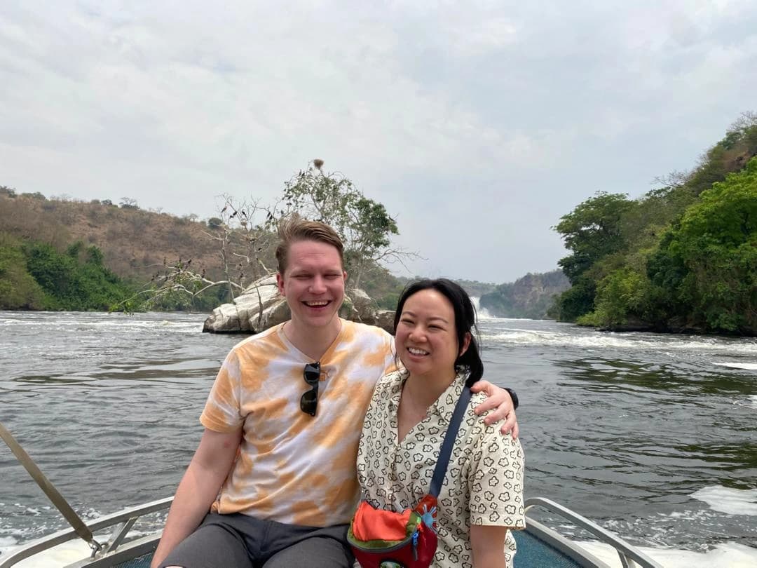 Romantic couple enjoying a scenic boat cruise to Murchison Falls in Uganda, admiring the powerful waterfall and lush wildlife along the Nile River.