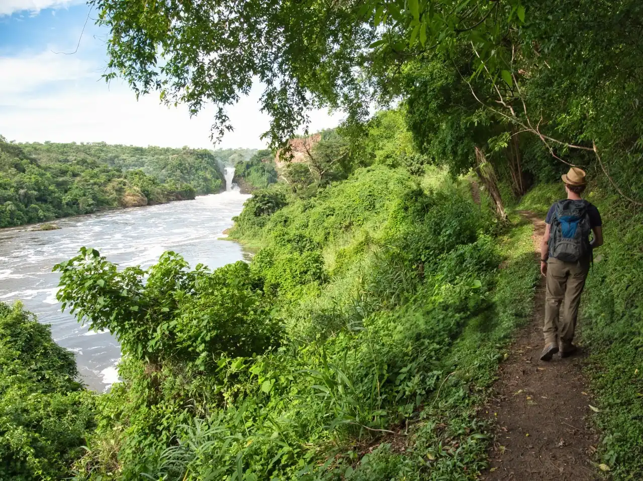 Man walking through rolling hills on the way to Murchison Falls National Park, symbolizing adventure and exploration during Queen Elizabeth vs Murchison Falls Safaris in Uganda.