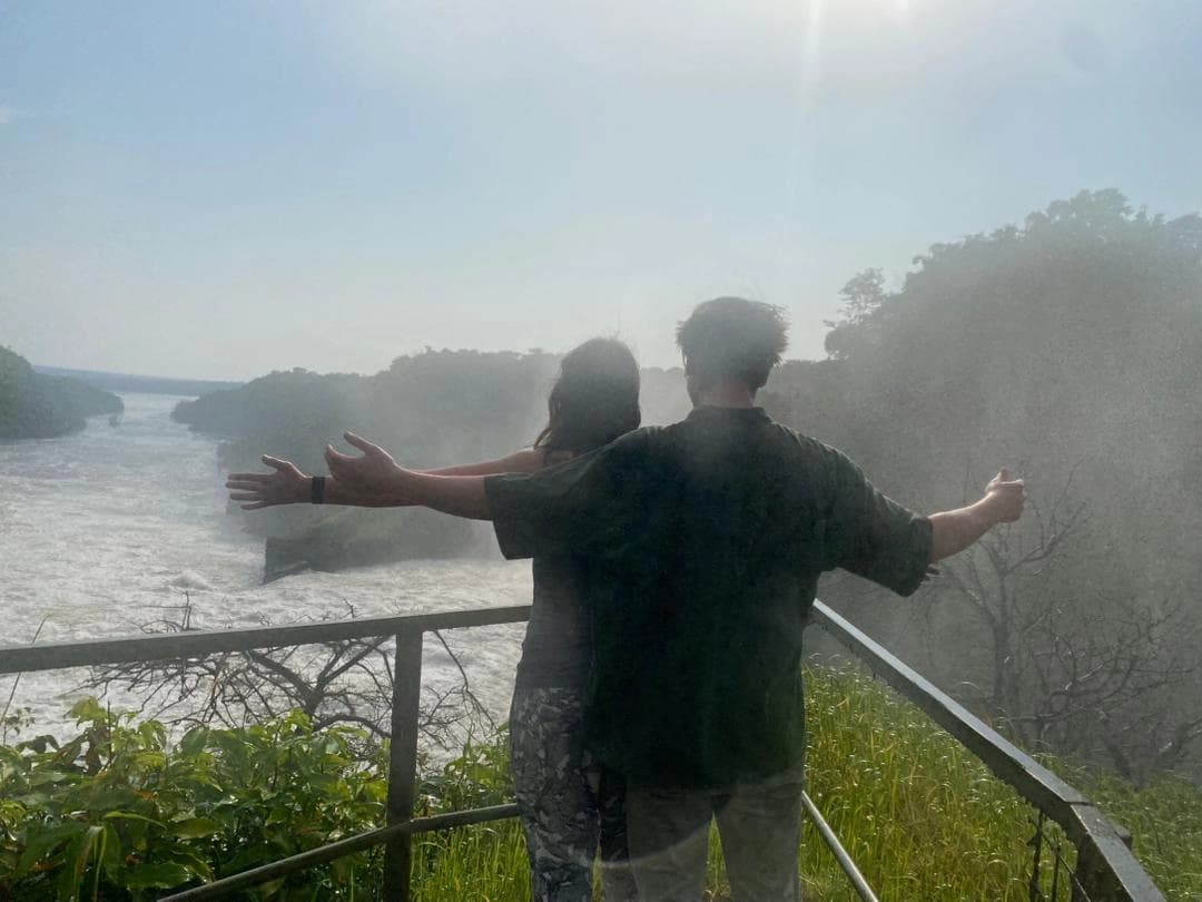 Couple standing with arms open overlooking Murchison Falls, comparing Queen Elizabeth vs Murchison Falls Safaris, romantic safari experience in Uganda.