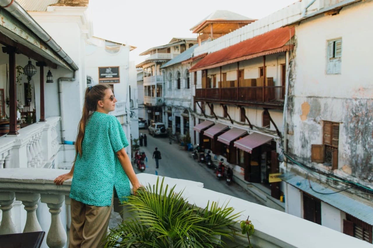 Traveler standing on a historic balcony overlooking Stone Town in Zanzibar at sunset — How To Visit & Experience Zanzibar: Ultimate Travel Guide.