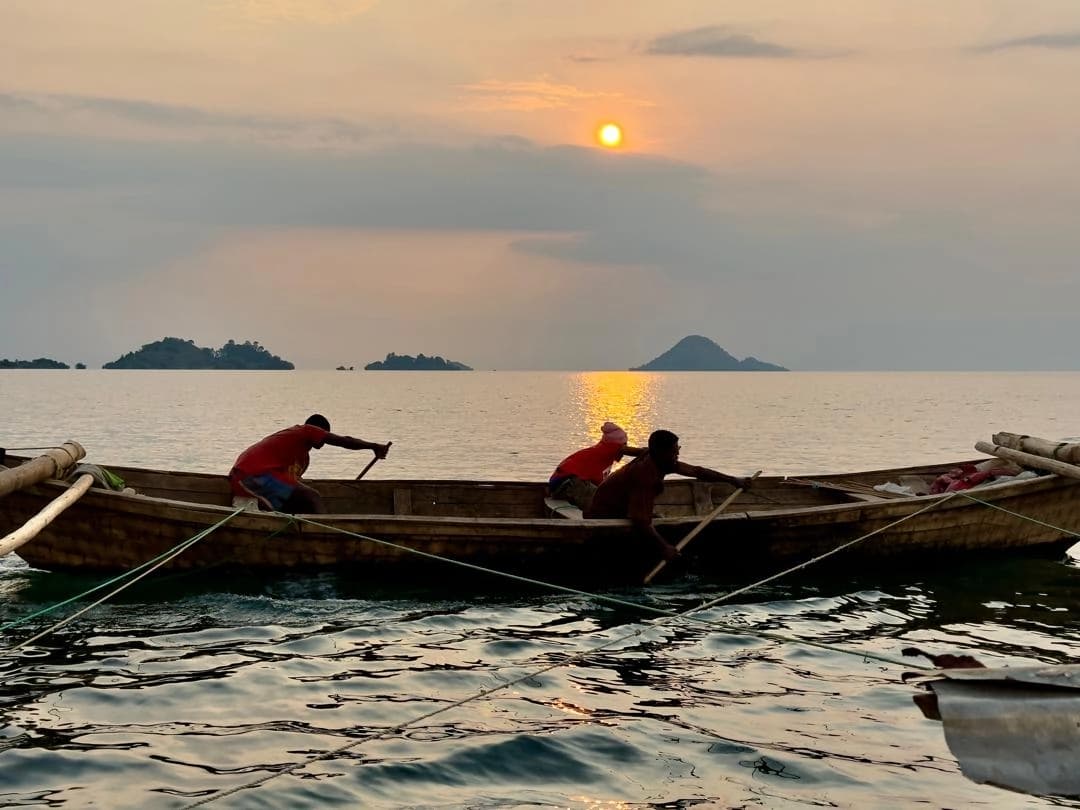 Local fishermen paddling a traditional boat on Lake Kivu along the scenic Congo Nile Trail in Rwanda, showcasing authentic local life and adventure tourism.