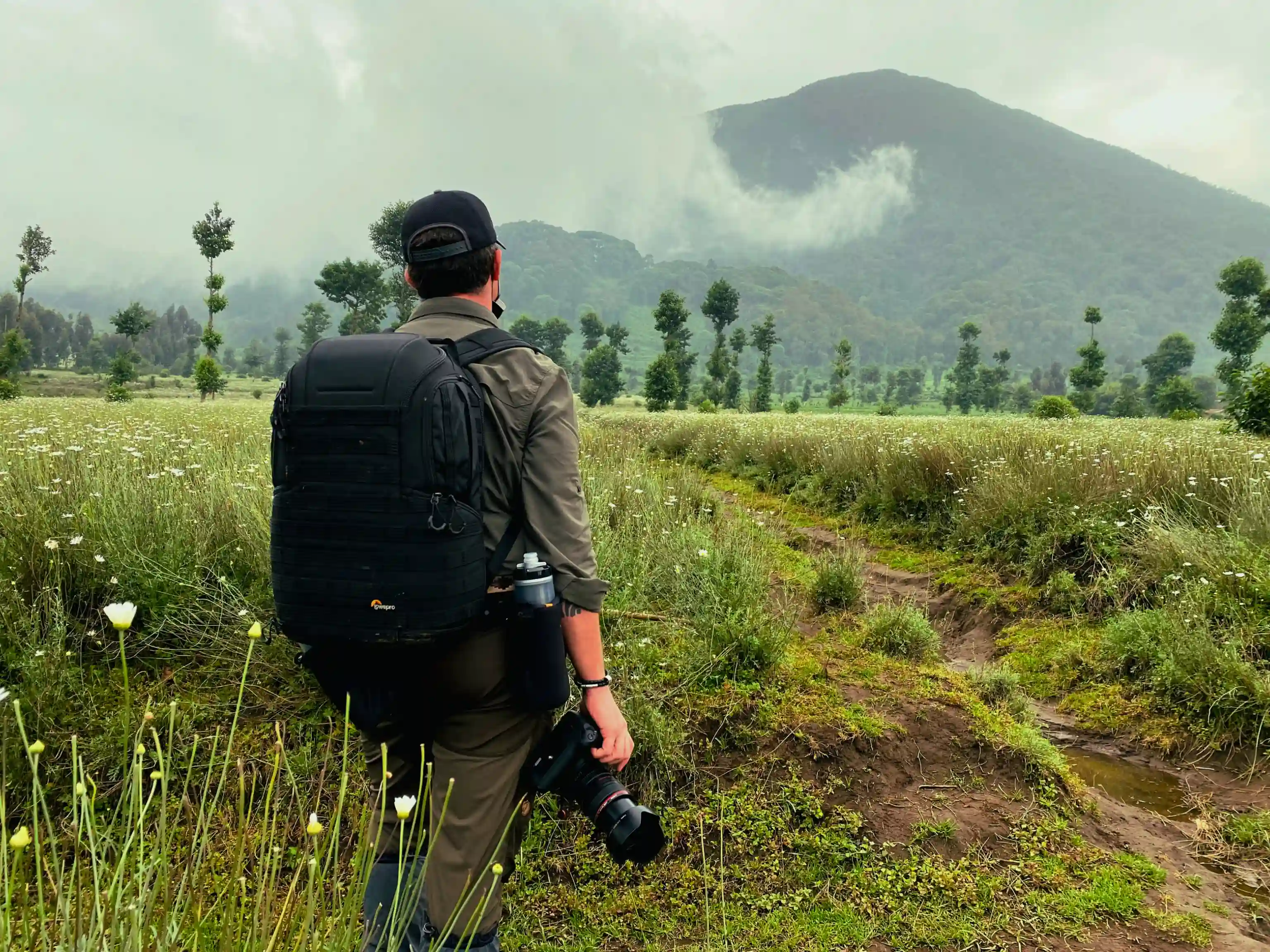 Photographer traveler capturing the majestic Volcanoes National Park mountains from a scenic pyrethrum farm in Rwanda, showcasing adventure and natural beauty.