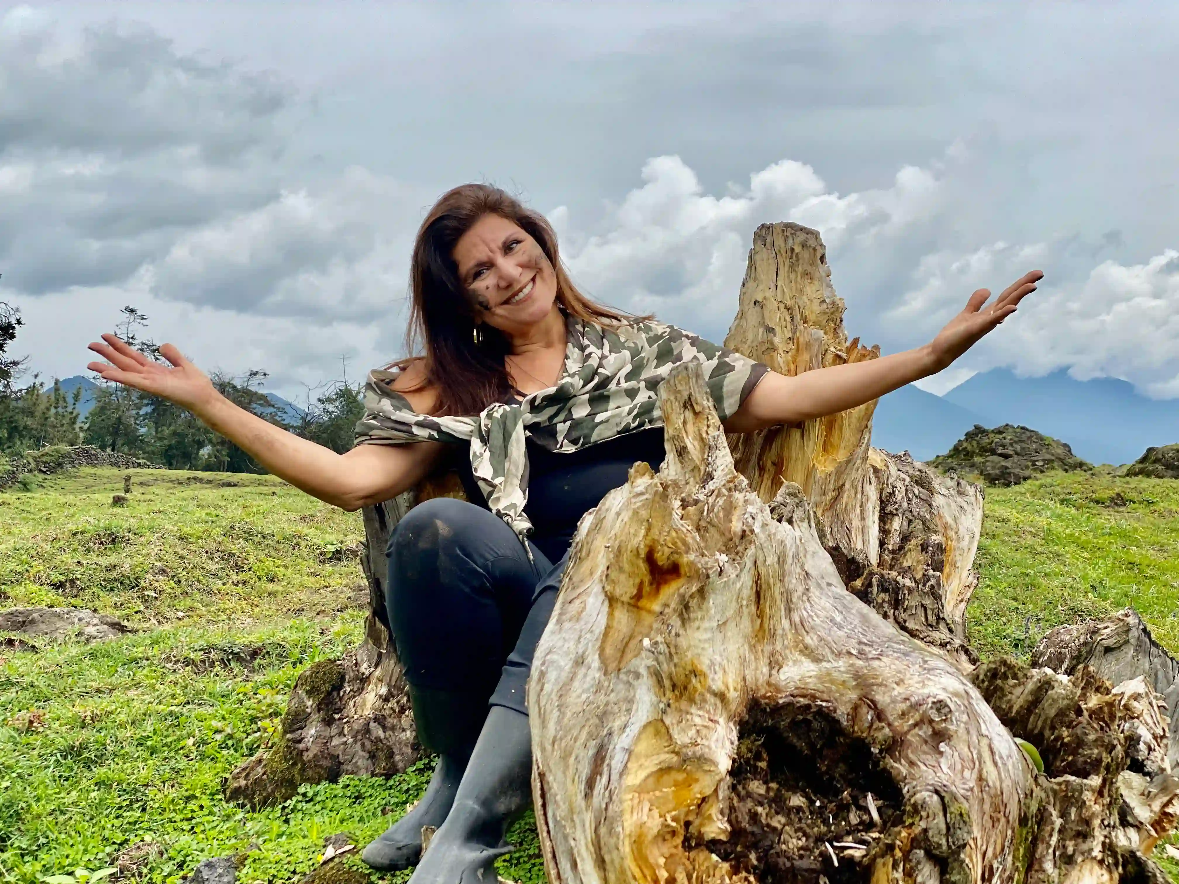 Solo woman traveler smiling with open arms in front of Volcanoes National Park mountains in Rwanda, embracing adventure and nature.